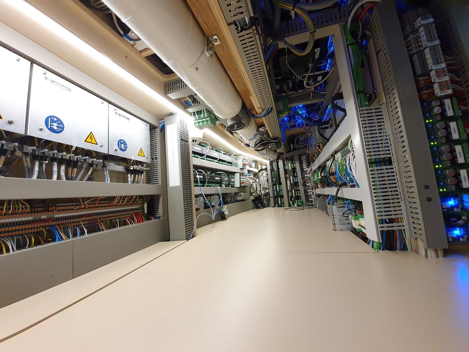 Technische ruimte aan boord met verlichte schakelkasten, kabelgoten en rijen DIN-rail modules